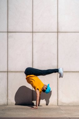 Kendine güveni tam genç bir çocuk sokakta beyaz duvara karşı break dans yapıyor..