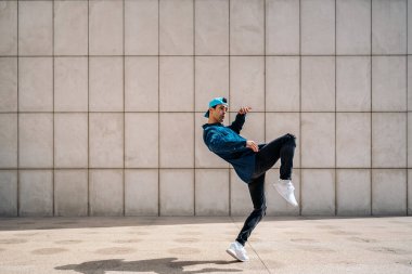 Yetenekli genç adam sokakta beyaz duvara karşı break dans yapıyor ve kameraya bakıyor..