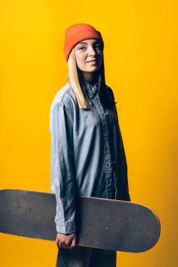 Stock photo of young expressive girl looking at camera in studio. She is holding a skateboard.