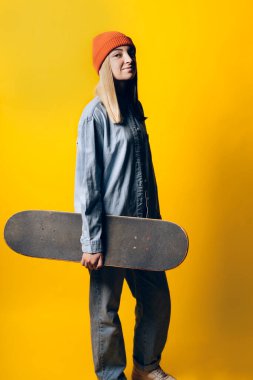 Stock photo of young expressive girl looking at camera in studio. She is holding a skateboard.