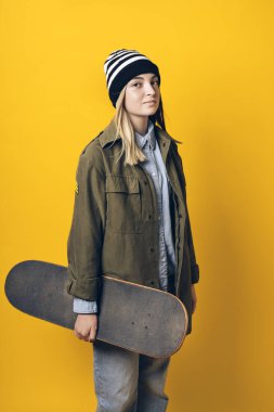 Stock photo of young expressive girl looking at camera in studio. She is holding a skateboard.