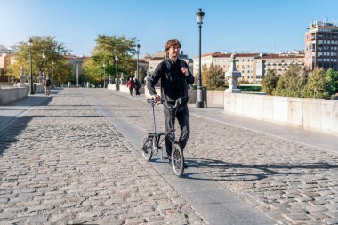 Stock photo of handsome man walking in the street carrying his detachable bike.