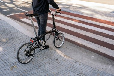Stock photo of unrecognized man waiting in a zebra crossing with his detachable bike.
