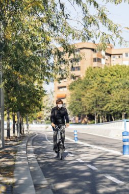 Yüz maskesi takan yakışıklı bir adamın sokağın ortasında sökülebilir bisikletini kullanırken çekilmiş resmi..