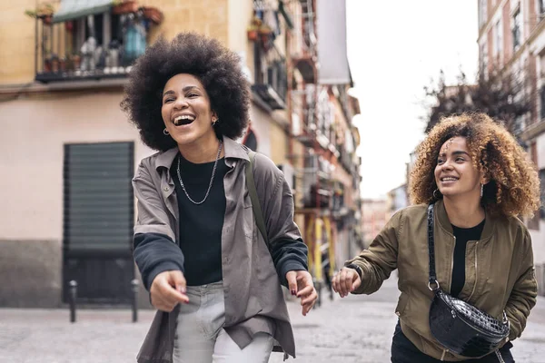 Stock photo of casual happy afro girls laughing and walking in the city.
