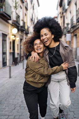 Stock photo of lovely afro girls hugging in the street and looking at camera.