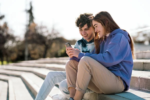 幸せな女の子と彼女の友人の階段に座って 携帯電話を使用しての写真 — ストック写真