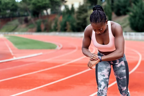 陸上競技場に立つアフリカ系アメリカ人のスプリンターのストック写真走り出す準備ができている彼女の時計と縛られた彼女の髪 — ストック写真