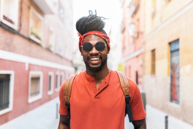 Rastalı ve bandanalı mutlu Afro-Amerikan bir çocuğun sokakta yürürken çekilmiş fotoğrafı..