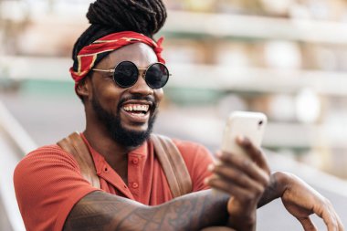 Rastalı ve bandanalı Afro-Amerikan bir çocuğun telefonunu kullanırken çekilmiş resmi. Gülüyor..