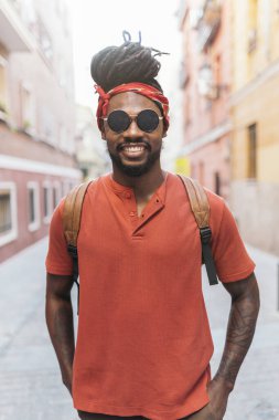 Rastalı ve bandanalı mutlu Afro-Amerikan bir çocuğun sokakta yürürken çekilmiş fotoğrafı..