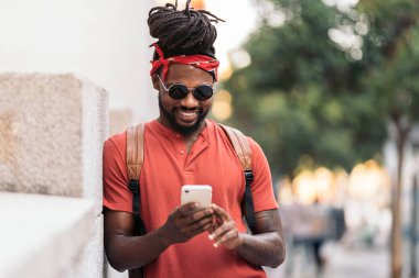 Rastalı ve bandanalı Afro-Amerikan bir çocuğun telefonunu kullanırken çekilmiş resmi. Gülüyor..