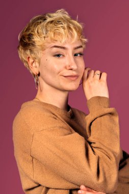 Kameraya bakıp pembe arka planda yüzüne dokunan etkileyici kızın stok fotoğrafı..