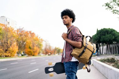 Şehirde yürüyen ve elinde uzun tahtasıyla gezen Afro bir çocuğun stok fotoğrafı..