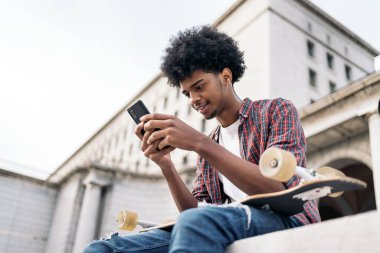 Şehirde eğlenen ve cep telefonunu kullanan yakışıklı Afrikalı çocuğun stok fotoğrafı..