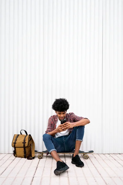 彼の長いボードの笑顔に座って 携帯電話を使用してクールなアフリカの男の子のストック写真 — ストック写真