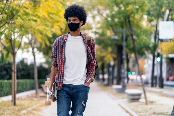 若いですアフロ少年のストック写真とともにロングボード歩行公園に着用フェイスマスクCoid19のために — ストック写真