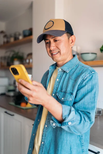 Вертикальное Фото Расслабленного Азиата Пьющего Кофе Пользующегося Мобильным Телефоном Дома Стоковая Картинка