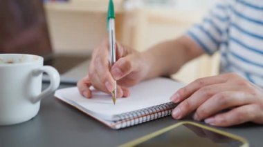 Ev ofisinin masasına elinde kahve fincanıyla oturup notlar yazan bir adamın ellerinin videosunu kapat.