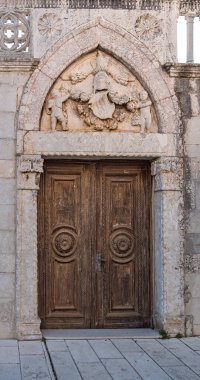 Rab, Hırvatistan - 19 Ağustos 2023: Taş kemer yolundaki tarihi ahşap kapı, karmaşık oymalar ve süslü taş motiflerle süslenmiş