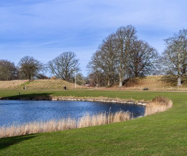 Landskrona, İsveç - 12 Şubat 2023: İsveç 'in güneyindeki Citadellas Şatosu' nda sakin bir kanal kayalık kıyı şeridi, yapraksız ağaçlar ve huzurlu doğal ortamında iyi bakılmış çimenler.