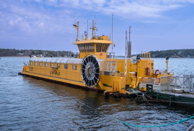 Vaxholm, İsveç - 11 Nisan 2023: Huzurlu Baltık Denizi kıyısı kale vagonları ve yolcularıyla çevrili tarihi bir kalenin yakınına canlı sarı bir feribot yanaştı