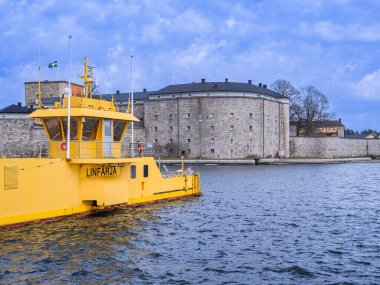 Vaxholm, İsveç - 11 Nisan 2023: Canlı sarı bir feribot tarihi bir kalenin yakınına yanaştı