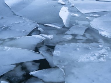 Suyun üzerinde yüzen çatlamış buz tabakalarının yakın çekimi, çeşitli şekil ve dokuları sergiliyor.