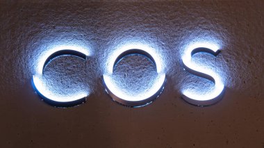 Zürih, İsviçre - 30 Aralık 2021: Modern tipografinin yer aldığı dokulu bir duvarda aydınlatılmış COS işareti.