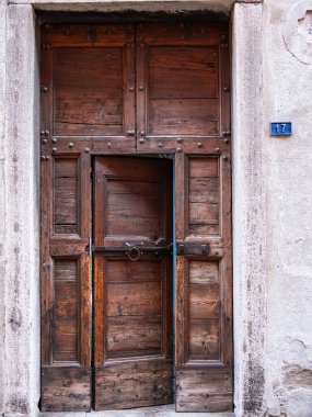 İçinde daha küçük bir kapı olan eski ahşap bir kapı, kırsal bir cazibe ve ustalık sergiliyor. Kapıda yıpranmış bir doku ve metal aksanlar var.