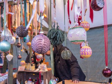 Stockholm, İsveç - 23 Aralık 2024: Parlak mücevherler ve desenli dekorasyonlar da dahil olmak üzere çeşitli şekil ve tasarımların yer aldığı bir pazar tezgahından sarkan renkli dekoratif süsler gösterisi