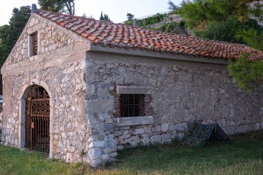Döşeme çatılı taştan bir bina, dövmeli demir kapı ve pencereleri var. Bina yeşilliklerle çevrili, yakınlarda da bir çadır var. Bu da açık havada huzurlu bir ortam olduğunu gösteriyor..
