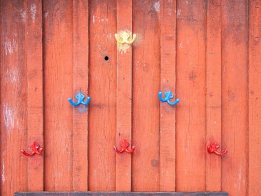 Turuncu ahşap bir duvara renkli kancalar yerleştirilmiş..