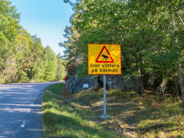 Vaxholm, İsveç - 6 Eylül 2024: İsveç 'in Stockholm takımadalarında yeşil ağaçlar ve dolambaçlı bir yol ile çevrili vahşi yaşam tehlikesi uyarısı.