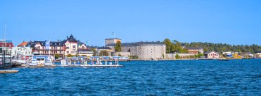 Vaxholm, İsveç - 6 Eylül 2024: Tarihi kale, tekne ve mavi gökyüzüne sahip bir kıyı kasabasının manzarası.