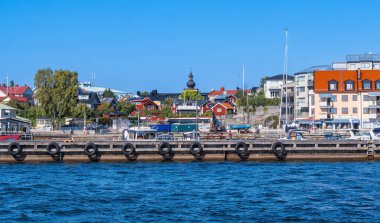 Vaxholm, İsveç - 6 Eylül 2024: Güneşli bir günde renkli binalar, bir iskele ve teknelerin bulunduğu kıyı kasabasının manzarası.