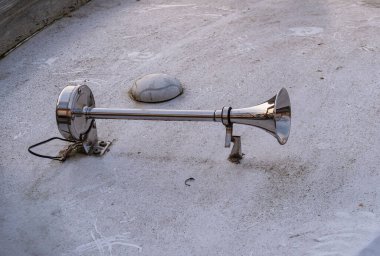 Metalik bir boynuz, desenli bir yüzeye monte edilmiş. Kornanın parlak bir sonu var ve bir kabloya bağlı. Bu da sinyal cihazının ya da alarm sisteminin bir parçası olabileceğini gösteriyor..