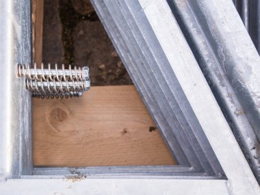 Metal inşaat malzemelerine yakın çekim, galvanize çelik açılar ve ahşap bir yüzeye sarılı bir yay..