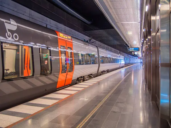 Malmö, İsveç - 9 Mart 2025: Gösterişli bir yeraltı istasyonunda, temiz bir platform ve parlak ışıklandırmayla modern bir tren. Trenin kendine özgü turuncu ve gri bir tasarımı var. Dijital ekranları var..