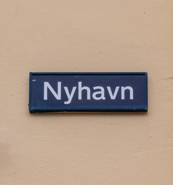 Kopenhag, Danimarka - 4 Nisan 2025: Bej bir duvarda 'Nyhavn' isminin yazılı olduğu bir sokak tabelası. İşaret, koyu mavi arkaplan ve beyaz harflerle dikdörtgen şeklinde..