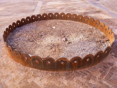 Kumlu bir yüzeye yerleştirilmiş, istiridyeli kenarlı dairesel metal bir yapı. İçi çakıl ve küçük taşlarla dolu. Dekoratif ya da işlevsel bir açık hava özelliği var..