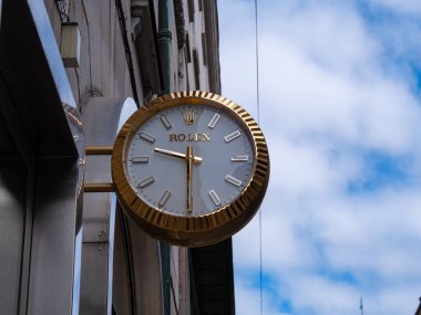 Stockholm, İsveç - 11 Mayıs 2025: Altın çerçeveli ve beyaz yüzlü, arka planda mavi gökyüzü ve bulutlu lüks bir Rolex saat.