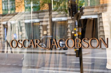 Stockholm, İsveç - 11 Mayıs 2025: 'Oscar Jacobson' adlı bir mağazanın vitrininde görüldü. Caddenin ve binaların yansıması camdan görülebilir..