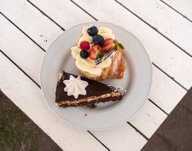 İki tatlı tabağı: kremalı bir dilim çikolatalı pasta ve krema ve çilek ve yabanmersinli taze meyvelerle dolu bir pasta..