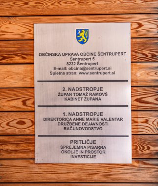 Sentrupert, Slovenya - 3 Temmuz 2025: Slovenya 'nın Sentrupert kentinin belediye yönetimi hakkında bilgi içeren ahşap bir duvara monte edilmiş metalik bir plaket. İsimleri ve başlıkları içeriyor..