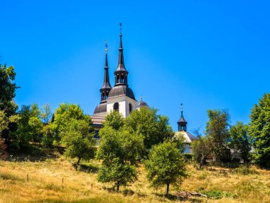 Sentrupert, Slovenya - 3 Temmuz 2025: Yeşillik ve açık mavi gökyüzü ile çevrili iki uzun kulesi olan resim gibi bir kilise. Bina mimari tarzların bir karışımını içeriyor..