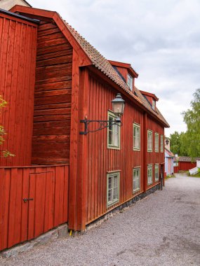 Sodertalje, İsveç - 6 Haziran 2025: Eğik çatılı ve yeşil pencere çerçeveli büyüleyici kırmızı ahşap bir ev. Binanın içinde bir fener var ve etrafı çakıl yollarıyla çevrili..