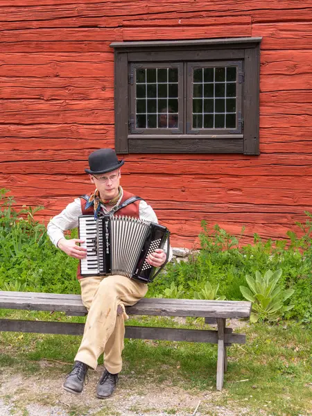 Sodertalje, İsveç - 6 Haziran 2025: Kırsal bir kırmızı binanın önündeki ahşap bankta oturan bir adam. Çalma İsveç 'te düzenlenen kutlamalarda gerçekleşti