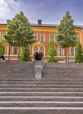Sodertalje, İsveç - 6 Haziran 2025: Geniş pencereli ve renkli yüzlü bir binaya çıkan bir dizi taş basamak. Çömlek bitkileri basamaklara yerleştiriliyor ve kentsel alana yeşillik ekleniyor..
