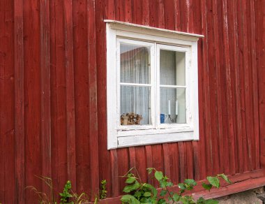Vaxholm, Sweden - 4 June 2025: A rustic red wooden wall with a white-framed window.